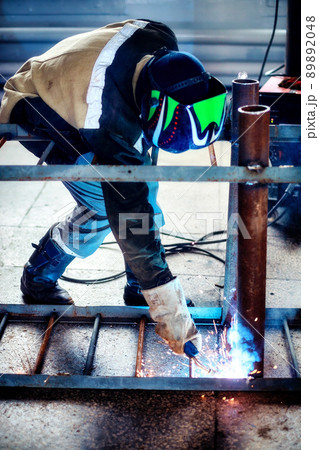 Professional welder in protective uniform and mask works in production hall. Authentic workflow Professional welder in protective uniform and mask works in production hall. Authentic workflow 89892048