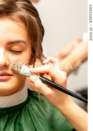 The makeup artist applies a cosmetic tonal foundation on the face using a makeup brush 89893064