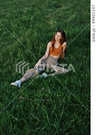 A woman lies on fresh spring green grass in a park without mosquitoes or ticks and enjoys relaxing while watching the sunset. The concept of safe outdoor recreation 89902247