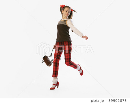 One young beautiful smiling girl, teenager in retro style outfit, fashion of 70s, 80s years standing isolated on white studio background with copyspace for ad. One young beautiful smiling girl, teenager in retro style outfit, fashion of 70s, 80s years standing isolated on white studio background with copyspace for ad. 89902873