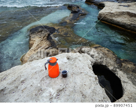 Orange thermos on the shore. Orange thermos on the shore. 89907451