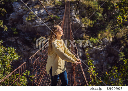 Woman tourist on Old rusty bridge. Attraction Long extreme suspension iron bridge across the river Moraca. Sights of Montenegro. Landmark Montenegro Woman tourist on Old rusty bridge. Attraction Long extreme suspension iron bridge across the river Moraca. Sights of Montenegro. Landmark Montenegro 89909074