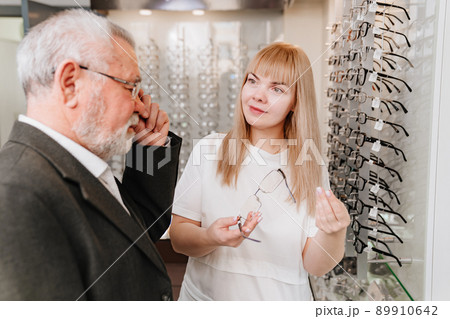 an elderly man with an ophthalmologist chooses glasses in the optics salon. 89910642