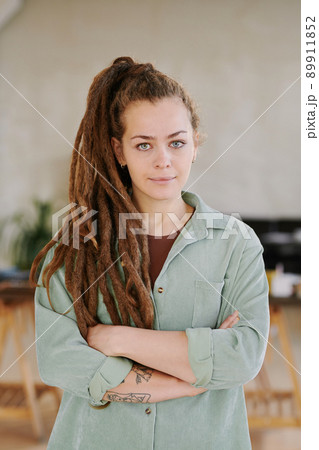 Portrait of serious young female SMM specialist in casual oversize shirt standing with crossed arms in modern office 89911852