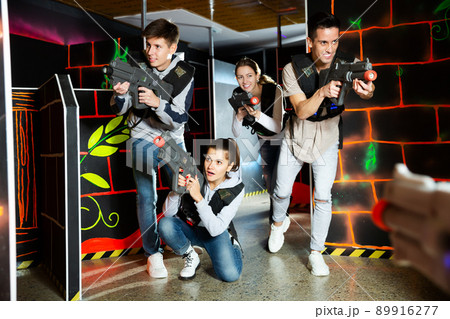Excited young people playing enthusiastically laser tag game two teams opposite each other in dark room Excited young people playing enthusiastically laser tag game two teams opposite each other in dark room 89916277