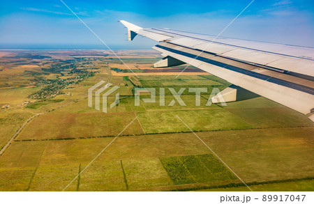View of airplane wing, blue skies and green land during landing. Airplane window view. 89917047