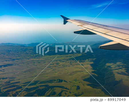 View of airplane wing, blue skies and green land during landing. Airplane window view. 89917049