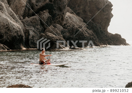 Side view foto of a man swiming and relaxing on the sup board. Sportive man in the sea on the Stand Up Paddle Board SUP. The concept of an active and healthy life in harmony with nature. 89921052