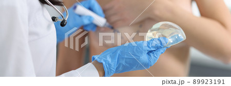 Doctor drawing preoperative marking on patient chest and holding implant closeup 89923191
