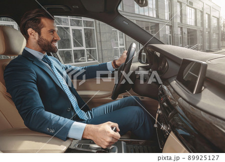 Laughing bearded male in suit is getting to work by automobile 89925127