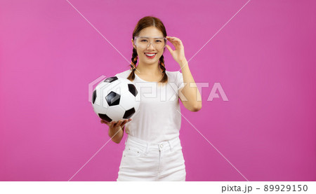 Portrait of Asian Young woman in white t-shirt over isolated pink background holding a soccer ball and looking at camera, football concept 89929150