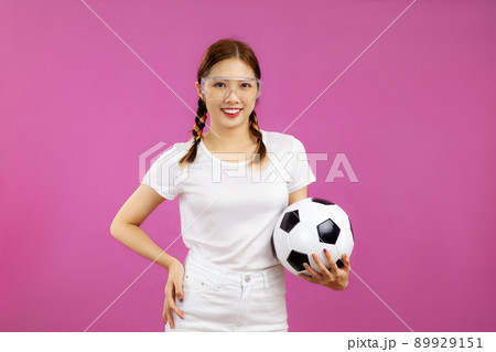Asian Young woman in white t-shirt over isolated pink background holding a soccer ball and looking at camera, football concept Asian Young woman in white t-shirt over isolated pink background holding a soccer ball and looking at camera, football concept 89929151