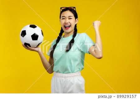 Portrait of Cheerful Asian woman holding a soccer ball isolated on yellow background, sport concept Portrait of Cheerful Asian woman holding a soccer ball isolated on yellow background, sport concept 89929157