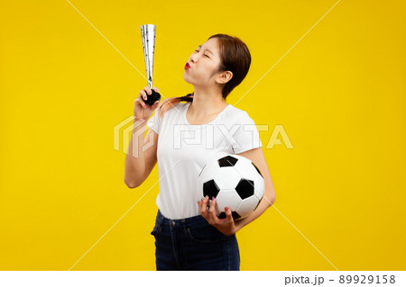 Cheerful Asian woman over isolated yellow background holding a soccer ball, sport concept 89929158
