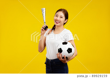 Joyful Asian woman holding a soccer ball and cheer horn isolated on yellow background, sport concept 89929159