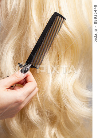 Barber holding comb on long curly blonde hair background closeup 89935449