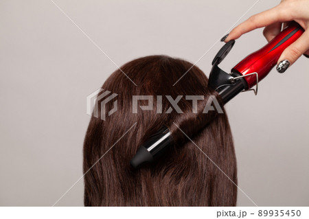 Brunette woman curling her hair with curler straightener Brunette woman curling her hair with curler straightener 89935450