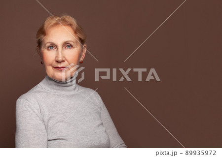 Mature woman in gray turtleneck on brown banner wall background with copy space Mature woman in gray turtleneck on brown banner wall background with copy space 89935972
