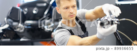 A male racer in a garage changes parts of a motorcycle 89936655