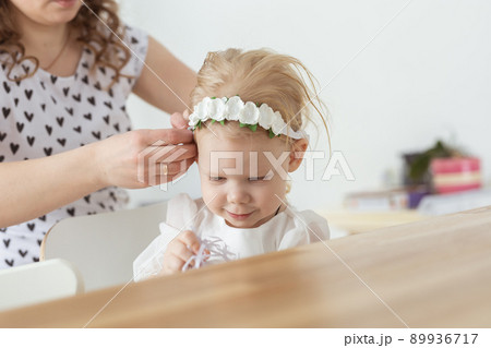 Mother helps her deaf baby daughter putting hearing aid in little girl's ear indoors - cochlear implant and innovative medical technologies in the treatment of deafness 89936717