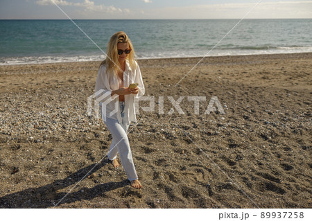 Full length shot of woman on vacation using phone while spending time on a beach Full length shot of woman on vacation using phone while spending time on a beach 89937258