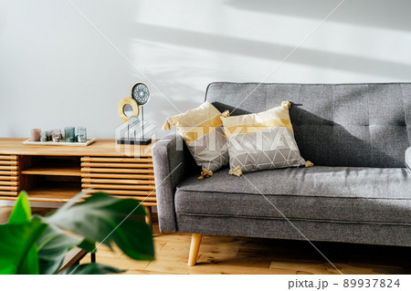 Stylish living room interior with designer console with decor and gray sofa with graphic pillows. White walls, green plants in the pots. Light wooden oak parquet. Modern Scandinavian style interior. 89937824