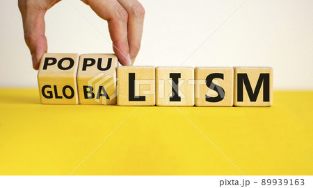Populism or globalism. Hand turns cubes and changes word 'globalism' to 'populism'. Beautiful yellow table, white background, copy space. Business and populism or globalism concept. Populism or globalism. Hand turns cubes and changes word 'globalism' to 'populism'. Beautiful yellow table, white background, copy space. Business and populism or globalism concept. 89939163