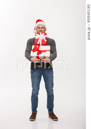 Christmas Concept - young handsome man with beard holding heavy presents with exhausted facial expression on white background. 89940190
