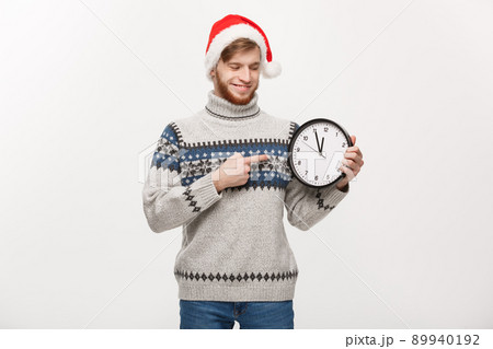 Holiday concept - Young handsome beard man pointing on white clock telling the time. Holiday concept - Young handsome beard man pointing on white clock telling the time. 89940192