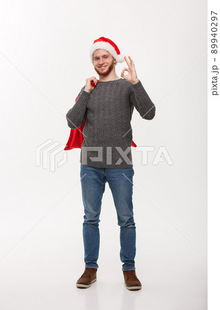 Christmas concept - Young confident smart man holding red big santa bag and giving ok sign. 89940297