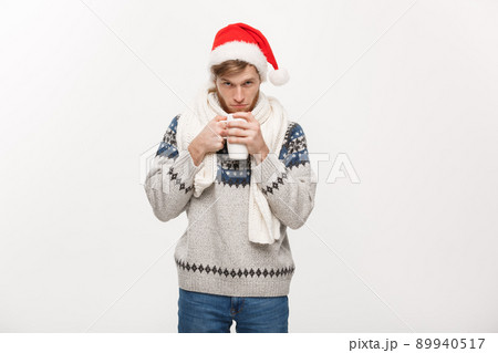 Christmas concept - Young beard man in sweater and santa hat holding a hot coffee cup isolated on white with copy space. 89940517