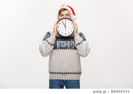 Holiday concept - Young handsome beard man hidden behind white clock over white studio background. 89940541