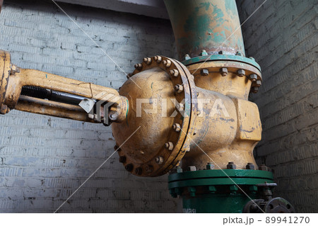 Close-up at pipeline valve which is using to control production process in the oil refinery plant. Selective focus at the valve handle wheel, Heavy industrial object photo. 89941270