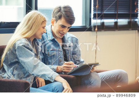 A couple sits in the hotel lobby, looking at a tablet computer. 89946809