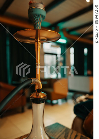 Hookah on table in lounge cafe. Shisha with burning coals at top. Leisure in oriental bar. Thick fume in flask of smoking apparatus. Hookah on table in lounge cafe. Shisha with burning coals at top. Leisure in oriental bar. Thick fume in flask of smoking apparatus. 89947260