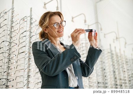 Woman chooses between two glasses in an optician's shop Woman chooses between two glasses in an optician's shop 89948518
