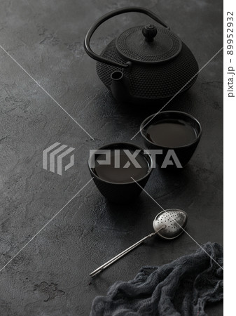 Chinese teapot with spoons and two cups and infuser on black background. 89952932