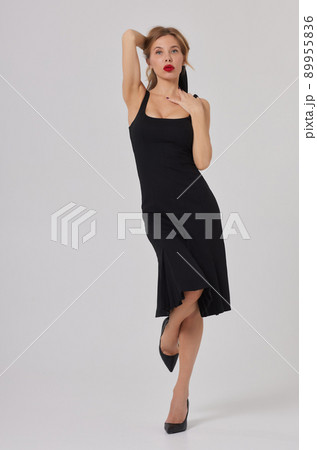 Beautiful stunning woman with red full lips, smokey eyes make up , shining perfect wavy hairs in elegant casual black dress posing on white background. 89955836