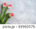 Three blooming pink tulips flowers with green leaves on gray concrete background flat lay with copy space for congratulations, advertising or design. Minimalism concept. 89960576