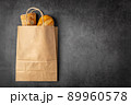 Disposable paper bag from a supermarket recyclable with whole baked loaves of bread flatlay on dark background with copy space. 89960578