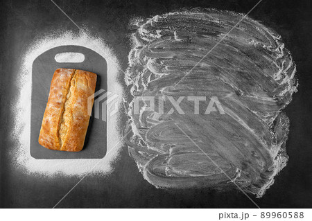 Top view of baking dark background withwith fresh whole loaf of bread and flour applied to place under the text and along contour of cutting board. 89960588