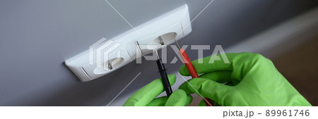 Hands in gloves measure the voltage in the outlet with a tool 89961746