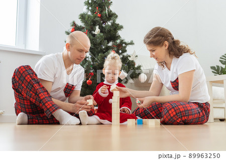 Toddler child with cochlear implant plays with parents under christmas tree - deafness and innovating medical technologies for hearing aid Toddler child with cochlear implant plays with parents under christmas tree - deafness and innovating medical technologies for hearing aid 89963250