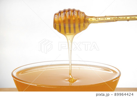 fresh honey dripping from a spoon into a transparent plate on a white background 89964424
