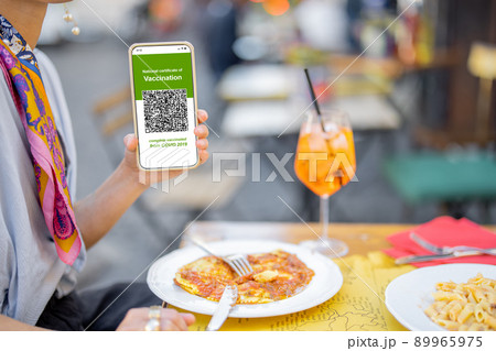 Woman showing vaccination certificate while sitting at outdoor restaurant Woman showing vaccination certificate while sitting at outdoor restaurant 89965975