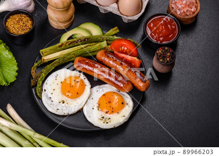 A delicious nourishing breakfast with fried eggs, sausages, asparagus, tomatoes, avocado, spices and herbs 89966203
