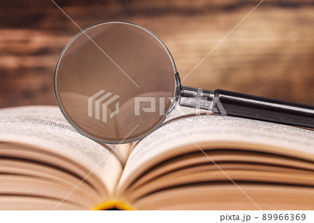 the magnifying glass is lying on an open book. space for text 89966369