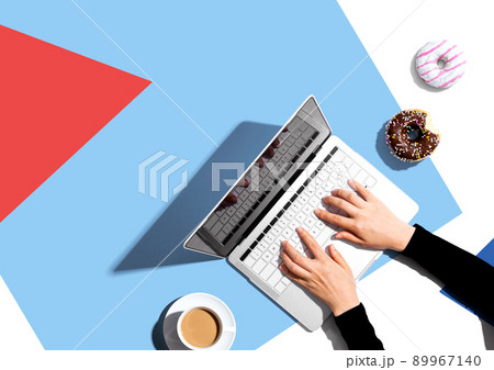 Person using a laptop computer with a donut and a cup of coffee 89967140
