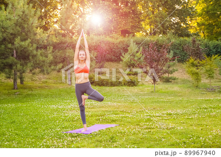 Cheerful young beautiful woman practicing and posing yoga in the park. tree pose. 89967940