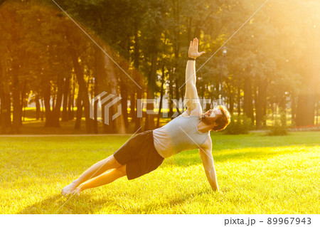 Strong young adult man doing yoga. Stay in plank on one arm. Looking up to the sky. Outdoor shot 89967943